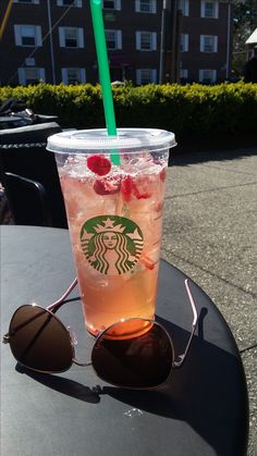 a starbucks drink sitting on top of a black table next to sunglasses and a green straw