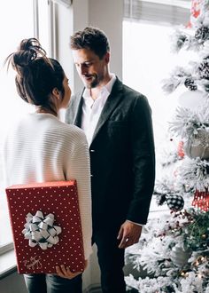 a man and woman standing in front of a christmas tree with presents under the tree