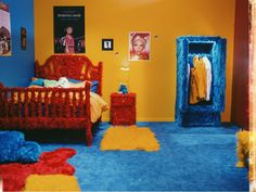 a bedroom decorated in bright colors with blue carpet and red bedding, yellow walls and pictures on the wall