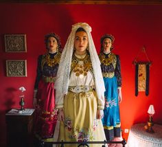 three women dressed in traditional clothing standing next to each other on a red room floor