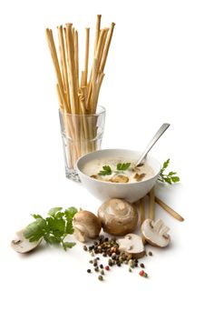 a bowl of soup with mushrooms, parsley and garlic sticks on the side next to it