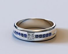 a white gold ring with blue sapphires on the sides and a princess cut diamond in the middle