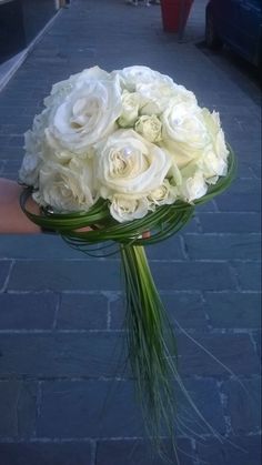 a bouquet of white roses is held on the street by someone's hand,