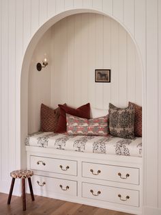 a white bench with lots of pillows on top of it and some drawers in front of it