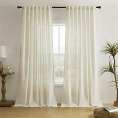 a living room with white curtains and a potted plant