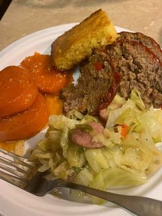 a white plate topped with meat, cabbage and carrots next to a knife and fork