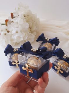 four small blue boxes with gold crosses and cross brooches on them are held by someone's hand