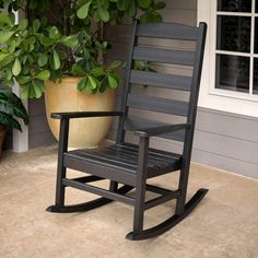 a black rocking chair sitting on top of a patio next to a potted plant