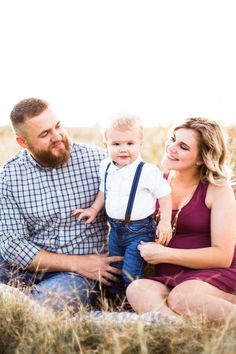 a man, woman and baby are sitting in the tall grass with their arms around each other