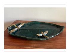 a green tray with two dragonflys sitting on it's sides and one is holding a leaf