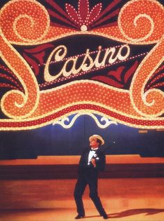 a man in a suit and hat standing under a casino sign with lights on it