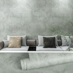 a couch with pillows on it in front of a concrete wall and plant behind the couch