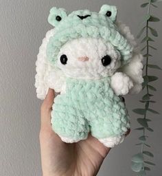 a hand holding a small crocheted stuffed animal in front of a white wall