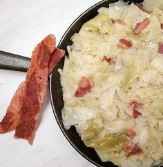 an iron skillet filled with cabbage and bacon next to a frying pan on a counter