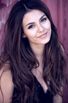 a woman with long brown hair and blue eyes smiling in front of a red door