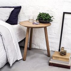 a bed with white sheets and pillows next to a small table with a potted plant on it