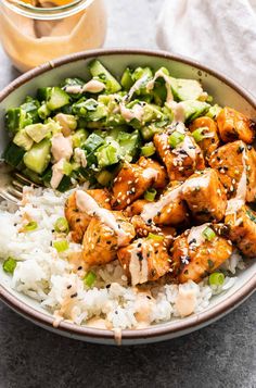 a bowl filled with chicken and rice next to a jar of dressing on the side