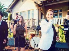 a group of people that are standing in front of a house playing instruments and singing