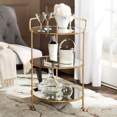 a glass and metal shelf with wine glasses on it in front of a chair, rug and window