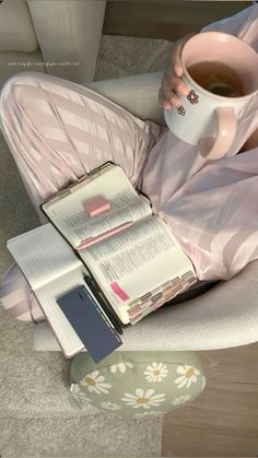 a woman sitting on the floor holding a cup of coffee and reading a book with her legs crossed