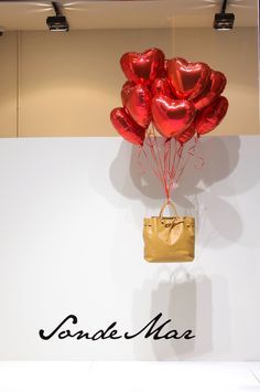 a bunch of red balloons floating in the air on top of a white wall next to a purse