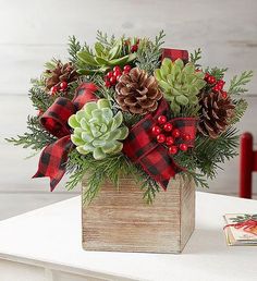 a christmas arrangement in a wooden box with pine cones, berries and greenery on the table