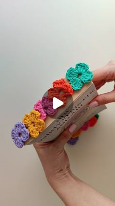 a person holding an open box with crochet flowers on it