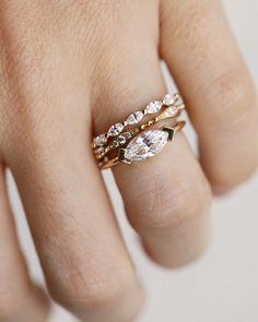 a woman's hand with three different rings on top of her ring and the middle one has an oval shaped diamond