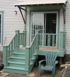 a green chair sitting in front of a white house next to a wooden porch and stairs