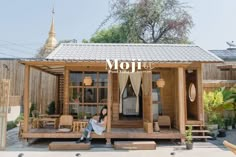 a woman sitting on the porch of a small wooden house with an awning over it