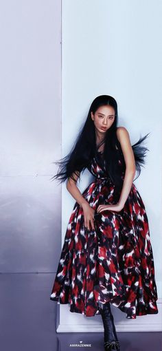 a woman sitting on top of a white wall wearing a red and black patterned dress