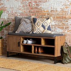 a wooden bench with shoes on it next to a brick wall and potted plant