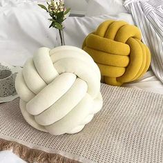 two decorative pillows on a bed next to a vase with a flower in it and a pillow that looks like a knot