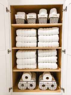 an organized linen closet with white towels, baskets and toilet paper on the bottom shelf