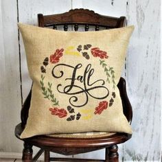 a pillow with the word fall on it sitting on a chair in front of a wooden wall