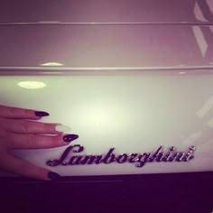 a woman's hand with black and white nail polish holding onto an automobile emblem