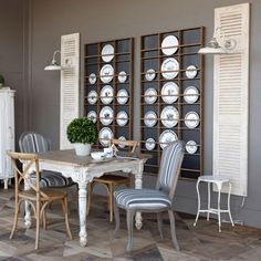 a dining room table with chairs and plates on the wall behind it in front of two shuttered windows