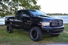 a black dodge ram truck parked in front of a body of water with trees and grass