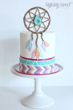 a white and blue cake with feathers on it's top, sitting on a stand