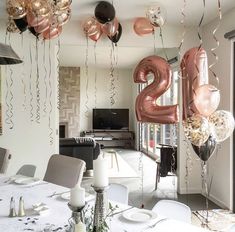 balloons and streamers are hanging from the ceiling above a table with white linens