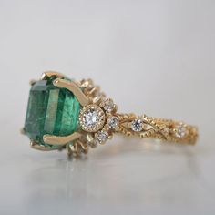 an emerald and diamond ring on a white surface