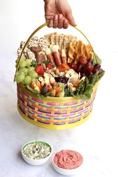 a person holding a basket full of food next to two small bowls with dips