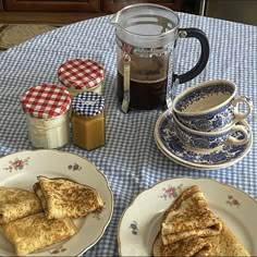 two plates with sandwiches on them sitting on a table next to cups and saucers