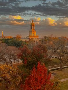 a clock tower towering over a city with trees in the foreground and clouds in the background