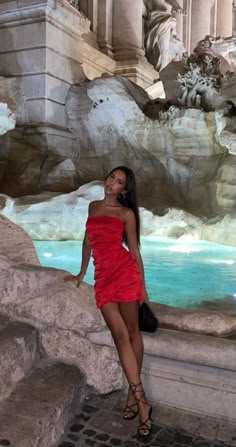 a woman in a red dress standing on some steps next to a fountain with water