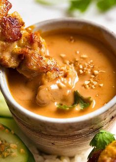 a close up of a bowl of soup on a plate with cucumbers and bread