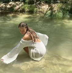 a woman sitting in the water with her back to the camera, wearing a white dress