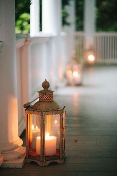 two lit candles sitting on the ground next to a white porch with columns and pillars