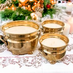 three gold dishes sitting on top of a table next to candles and christmas tree in the background