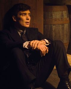 a man in a suit and tie sitting on the ground next to some wooden barrels